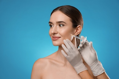 Beautiful woman getting facial injection on light blue background. Cosmetic surgery