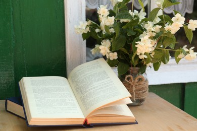 Books and beautiful jasmine flowers on wooden table near window outdoors