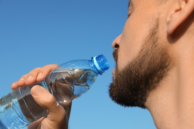 Photo of Man drinking water against blue sky on hot summer day, closeup. Refreshing drink