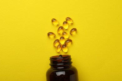 Photo of Overturned bottle with dietary supplement capsules on yellow background, flat lay