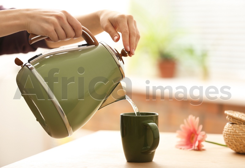 Woman pouring water into ceramic cup at table indoors, closeup