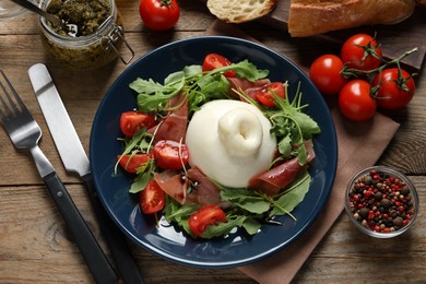 Delicious burrata salad with tomatoes, prosciutto and arugula served on wooden table, flat lay