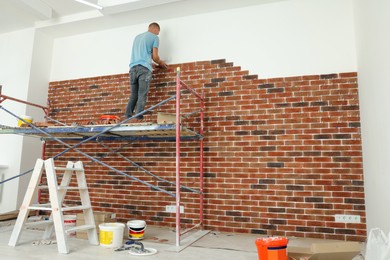 Professional builder gluing decorative bricks on wall in room. Tiles installation process