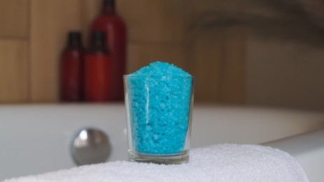 Glass with sea salt and fluffy towel on bath