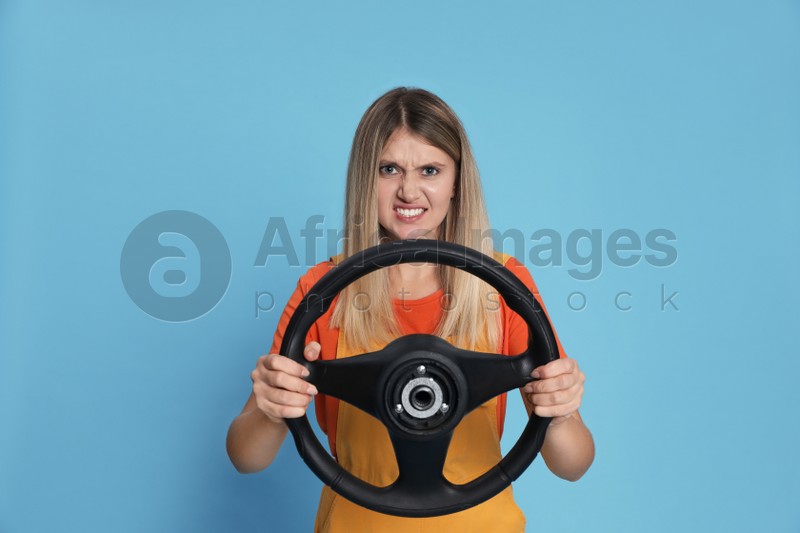 Emotional young woman with steering wheel on light blue background