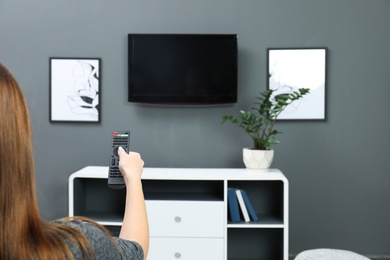 Woman switching channels on plasma TV with remote control at home