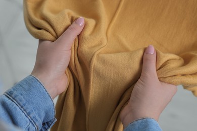 Photo of Woman touching clothes made of soft yellow fabric indoors, closeup