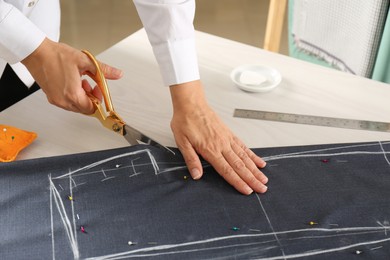 Photo of Seamstress cutting fabric following chalked sewing pattern at table in workshop, closeup