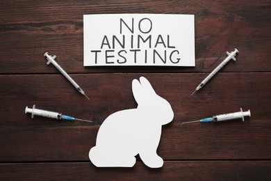 Card with text No Animal Testing, figure of rabbit and syringes on wooden table, flat lay