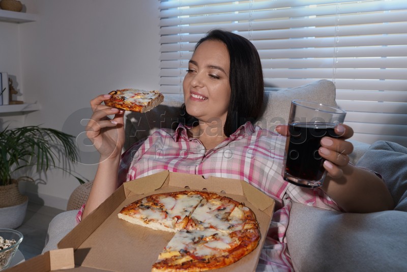 Happy overweight woman with pizza and cola on sofa at home