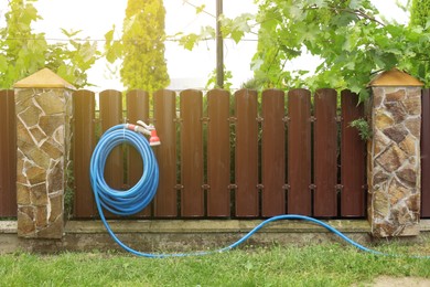 Watering hose with sprinkler hanging on wooden fence in garden, space for text