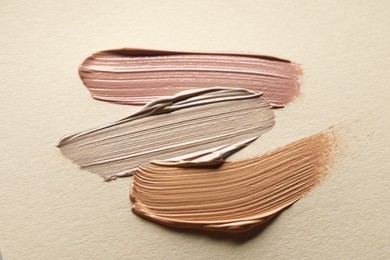 Different shades of liquid foundation on beige background, top view