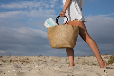 Woman carrying bag with beach towel on sand, closeup