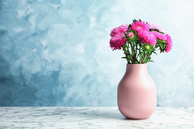 Vase with beautiful aster flower bouquet on table against color background. Space for text