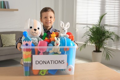 Cute little boy holding donation box with toys at home, space for text