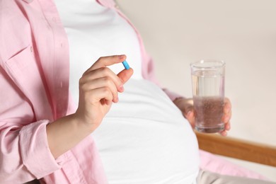 Pregnant woman taking pill in armchair, closeup. Space for text