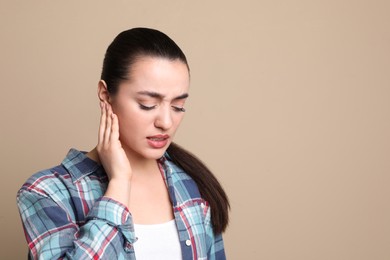 Young woman suffering from ear pain on beige background. Space for text