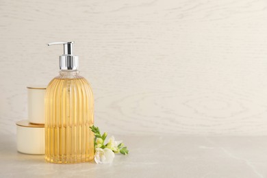 Stylish soap dispenser, flower and jars on light table. Space for text