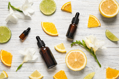 Flat lay composition with bottles of citrus essential oil on white wooden background