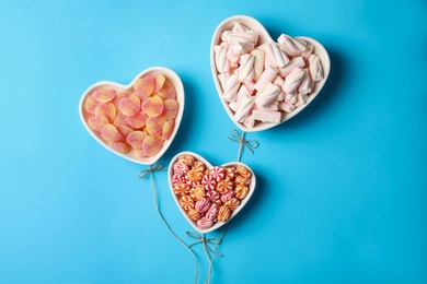 Twine near heart shaped bowls full of sweets imitating balloons on light blue background, top view