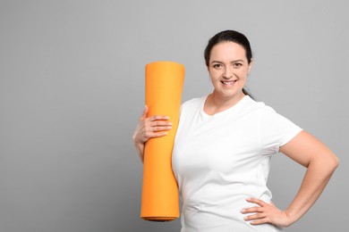 Photo of Happy overweight woman with yoga mat on grey background, space for text