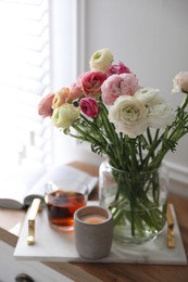 Bouquet of beautiful ranunculuses, candle and tea on cabinet in room