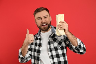 Young man with delicious shawarma on red background