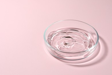 Petri dish with liquid on pale pink background, space for text