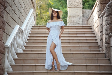 Photo of Beautiful young woman in stylish light blue striped dress and hat on stairs outdoors