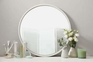 Photo of Stylish round mirror on dressing table with cosmetic products and flowers