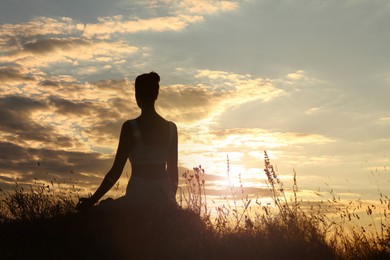 Silhouette of woman meditating outdoors at sunset, back view. Space for text
