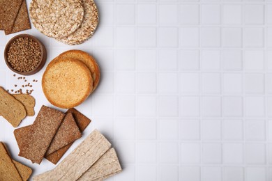 Rye crispbreads, rice cakes and rusks on white checkered table, flat lay. Space for text
