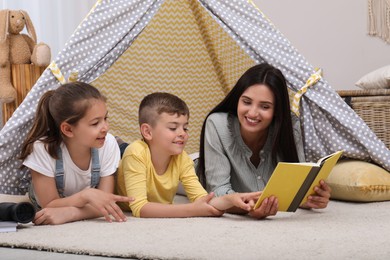 Mother with children reading book in wigwam at home