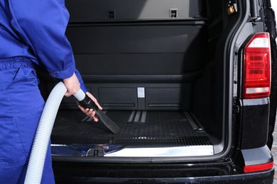 Worker using vacuum cleaner in automobile trunk at car wash, closeup