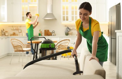 Professional janitor in uniform vacuuming sofa indoors