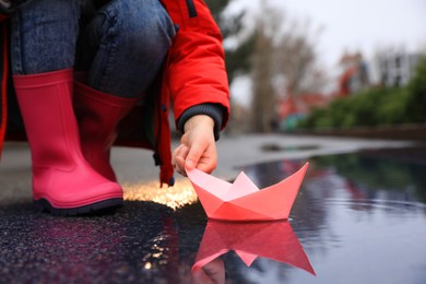 Little girl playing with paper boat near puddle outdoors, closeup