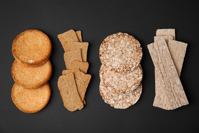 Rye crispbreads, rice cakes and rusks on black background, flat lay