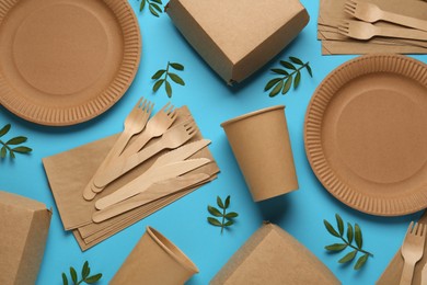 Paper and wooden tableware with green twigs on turquoise background, flat lay. Eco friendly lifestyle