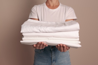 Woman holding stack of clean bed linens on beige background