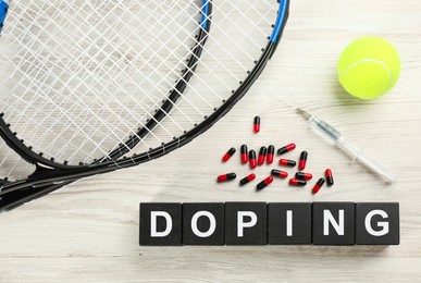 Photo of Black cubes with word Doping, tennis rackets, ball and drugs on white wooden background, flat lay