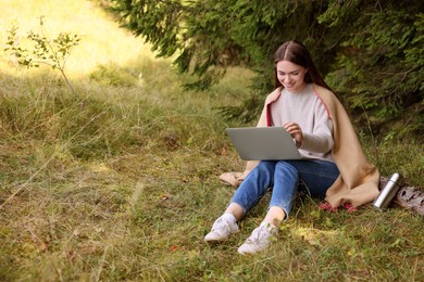 Photo of Young woman working on laptop in forest, space for text