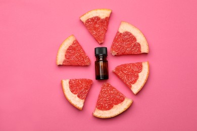 Bottle of citrus essential oil and fresh grapefruit slices on pink background, flat lay