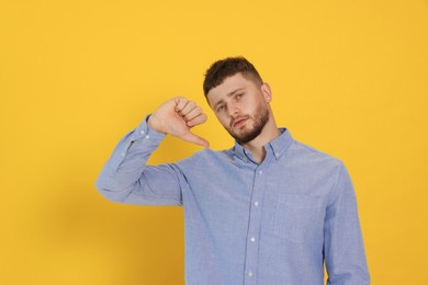 Young man showing thumb down on orange background