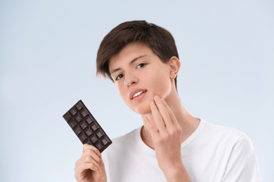 Teenage boy with acne problem holding chocolate on light background. Skin allergy