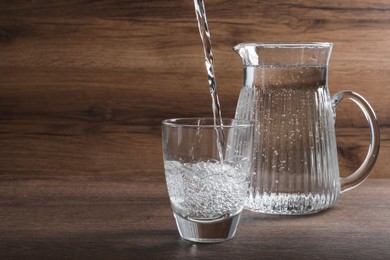 Pouring soda water into glass near jug on wooden table. Space for text