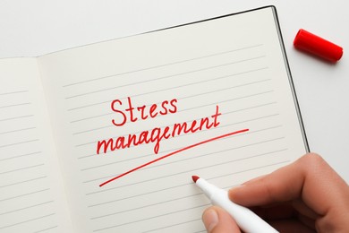 Photo of Man writing words Stress Management in notebook on white background, top view