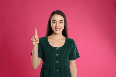 Woman showing number one with her hand on pink background