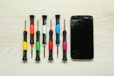 Damaged smartphone and repair tools on wooden background, flat lay
