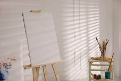 Wooden easel with empty canvas and brushes in art studio