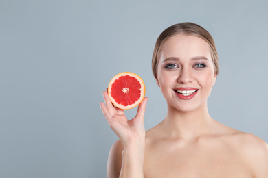 Young woman with cut grapefruit on grey background, space for text. Vitamin rich food